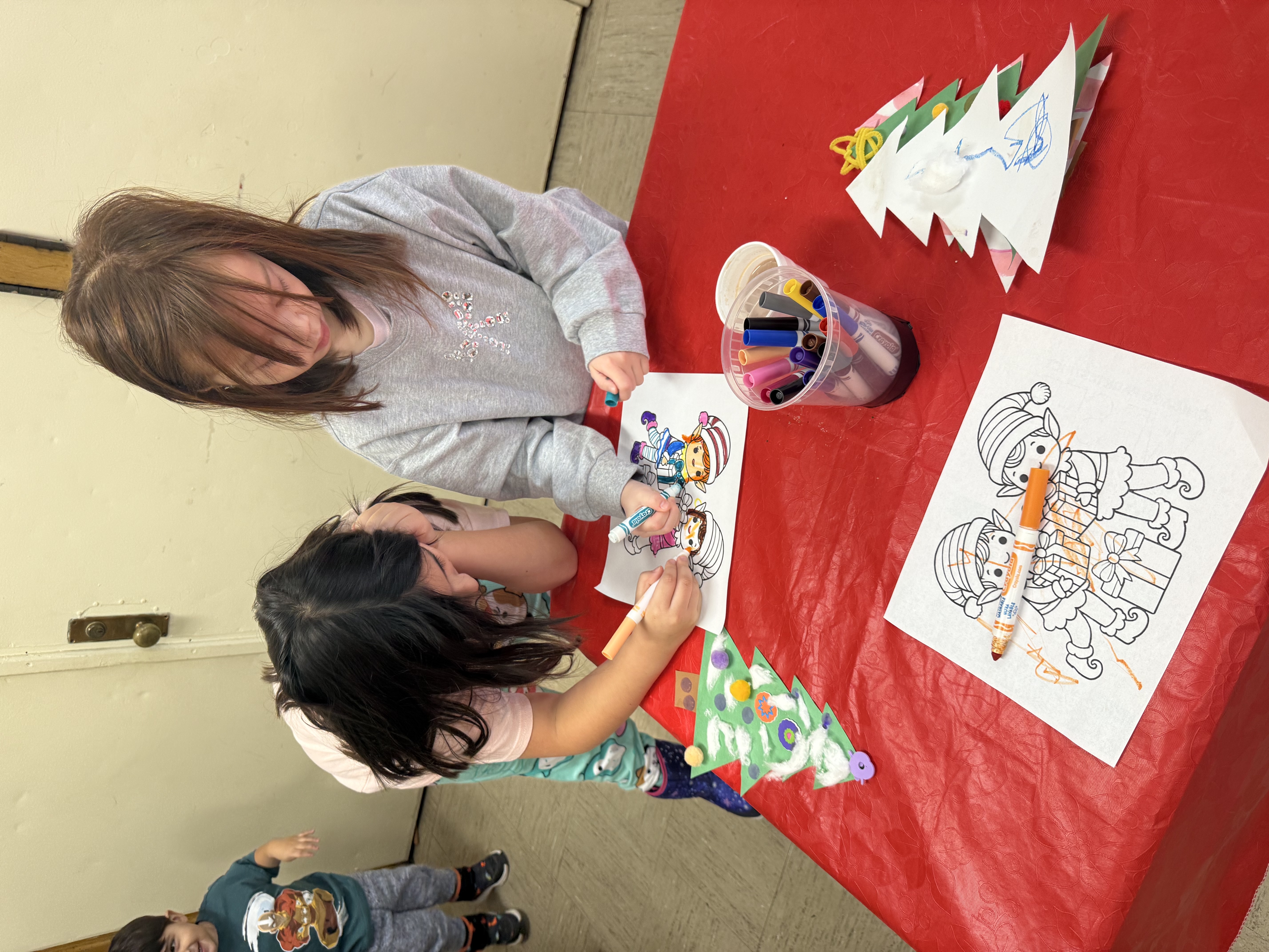 Two girls coloring and crafting at a red table.